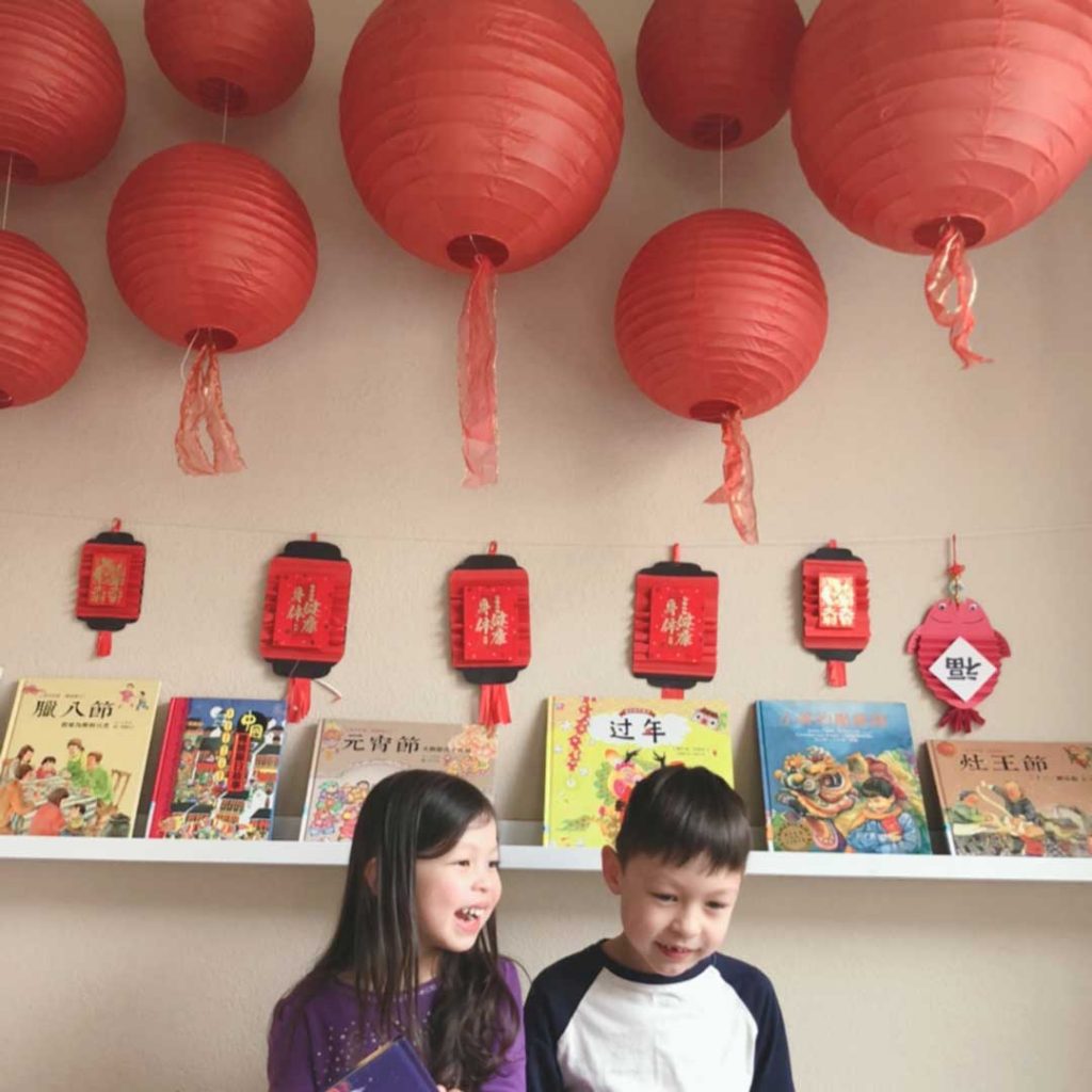 happy children sitting under red paper lanterns and chinese new year decorations